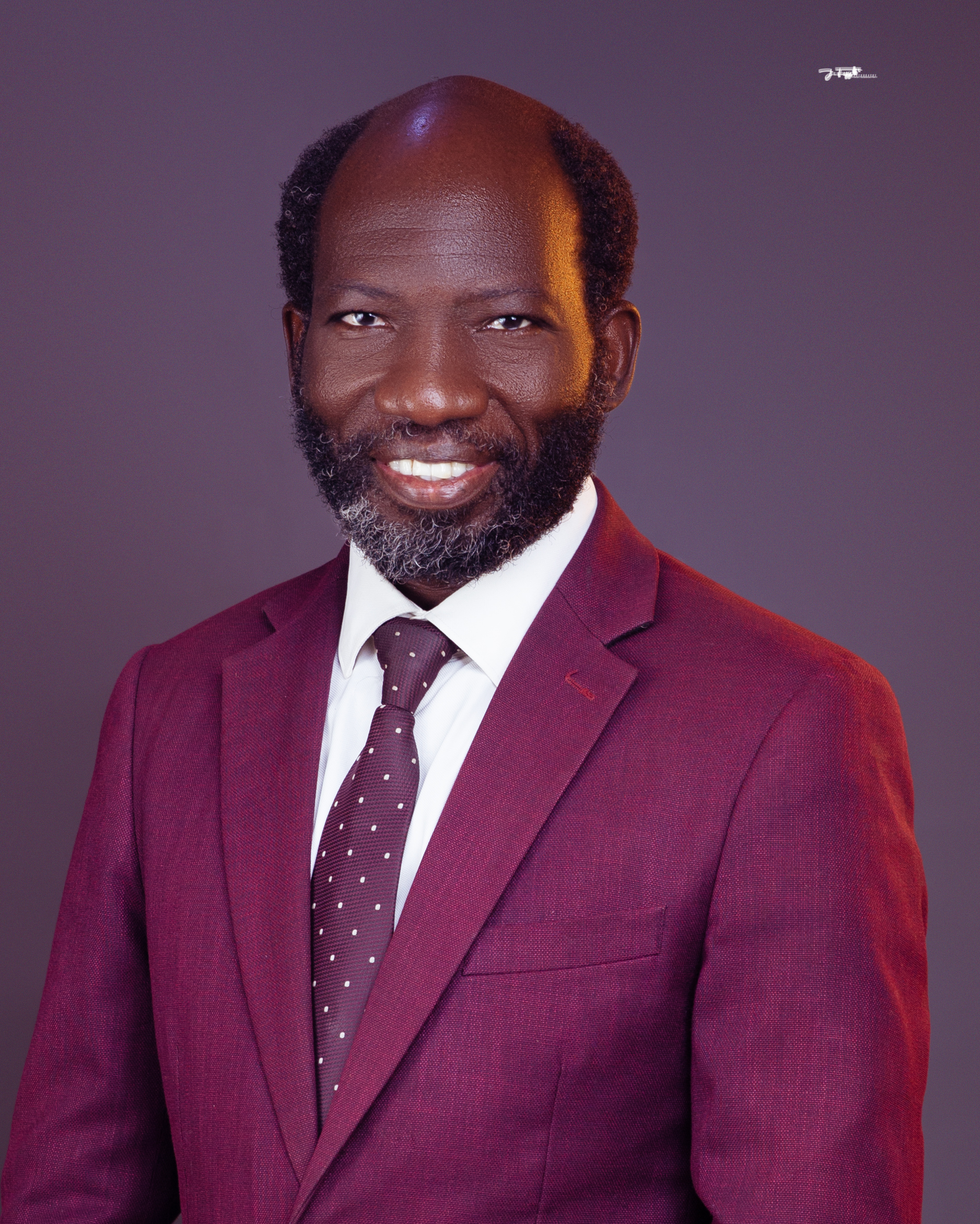 Gideon Mutum standing outdoors in a brown jacket with a blurred natural background